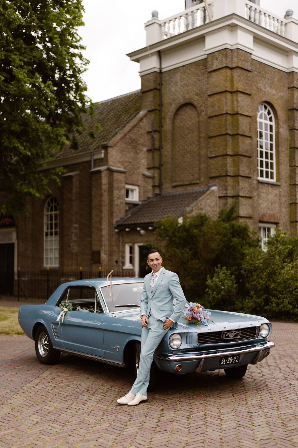 Bruidspaar bij de klassieke lichtblauwe Ford Mustang voor een landgoed